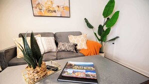 A living room with a grey sofa, a coffee table with a book titled '50 States 500 Day Hikes', and a large green plant. - Downtown Gem Close to Everything (Little Rock)