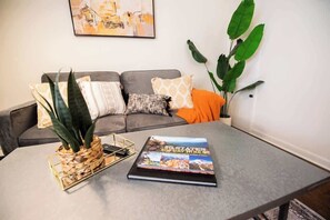 A living room with a grey sofa, a coffee table with a book titled '50 States 500 Day Hikes', and a large green plant. - Downtown Gem Close to Everything (Little Rock)