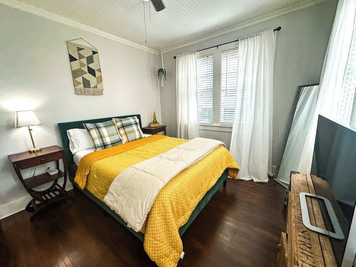 A bedroom with a bed, a nightstand, a lamp, a wall decoration, and a window with curtains.