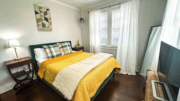 A bedroom with a bed, a nightstand, a lamp, a wall decoration, and a window with curtains.