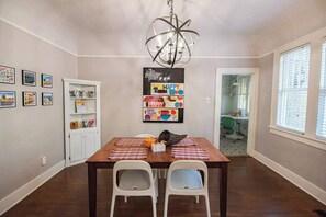 A dining room with a wooden table, white chairs, a chandelier, and a wall with framed pictures and a 'Happy Birthday' poster. - Spacious Home with Big Backyard (Little Rock)