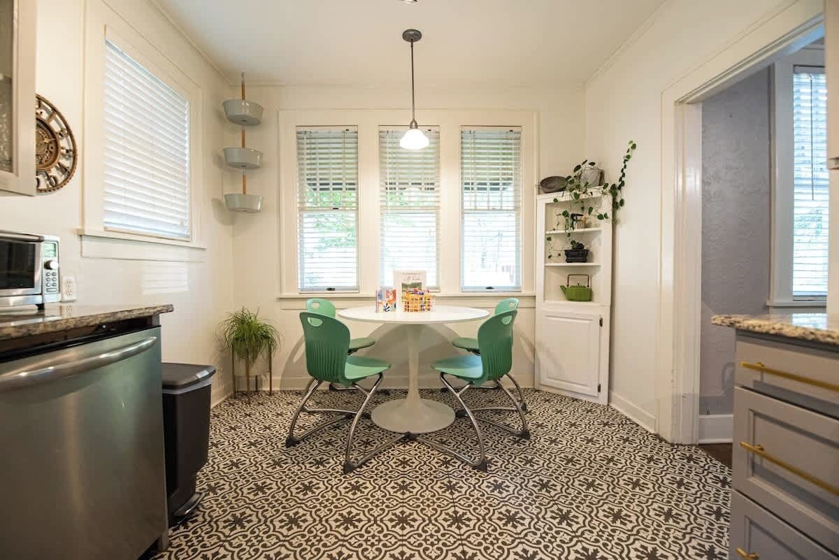 A kitchen with a patterned floor, a dining table with chairs, a microwave, and a trash bin.