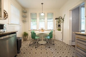 A kitchen with a patterned floor, a dining table with chairs, a microwave, and a trash bin. - Spacious Home with Big Backyard (Little Rock)