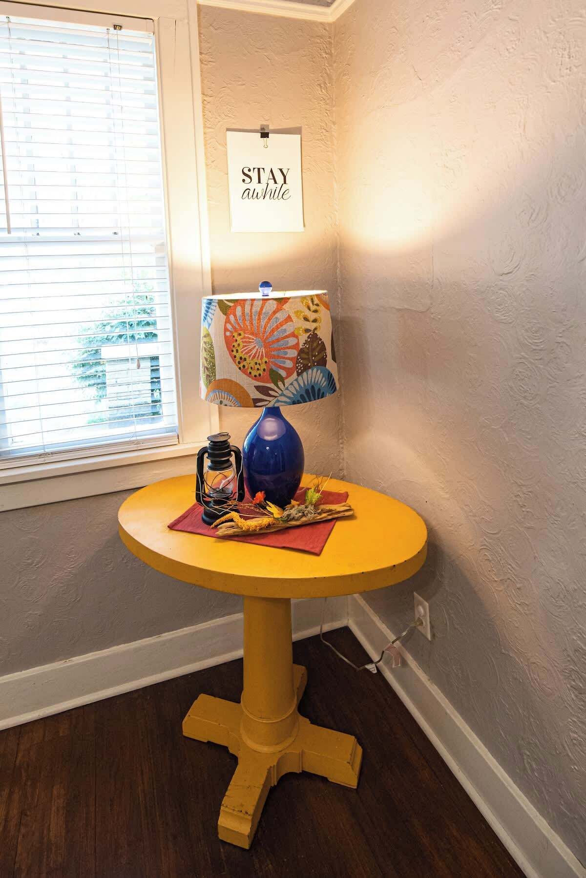 A yellow table with a blue vase, a lantern, and a decorative item on a window sill.