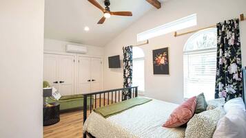 A bedroom with a bed, a ceiling fan, a window with curtains, and a wall-mounted TV.