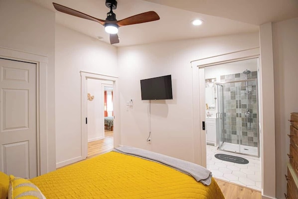 A bedroom with a bed, a ceiling fan, a TV, and a shower area.