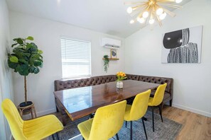 Un coin repas avec une table en bois, des chaises jaunes, un banc et une plante en pot.