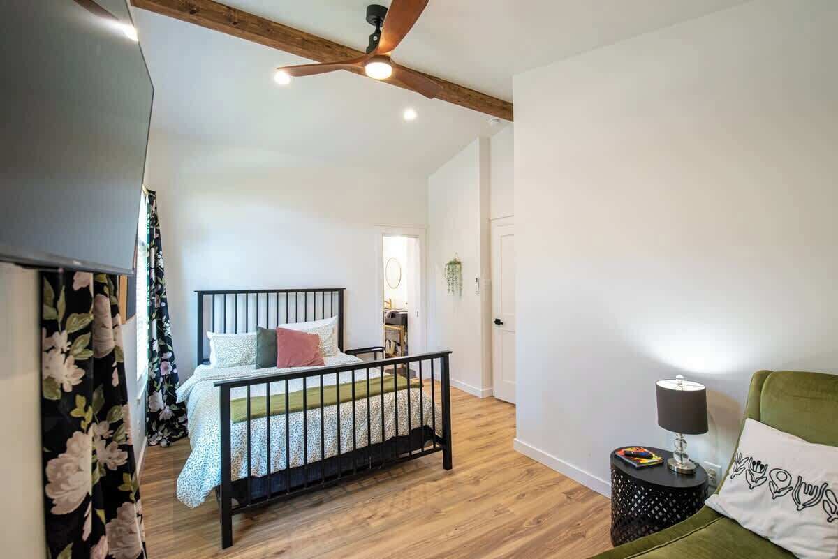 A bedroom with a bed, a ceiling fan, a bedside table with a lamp, and a green chair.