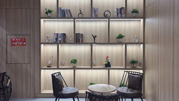 A modern room with a wooden panel wall, a bookshelf with books and decorative items, two leather chairs, and a round table. - V Tour Hotel (Shanghai)