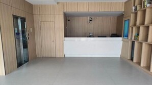 A reception area with a wooden reception desk, a glass elevator, and a wall-mounted shelf with items. - V Tour Hotel (Shanghai)