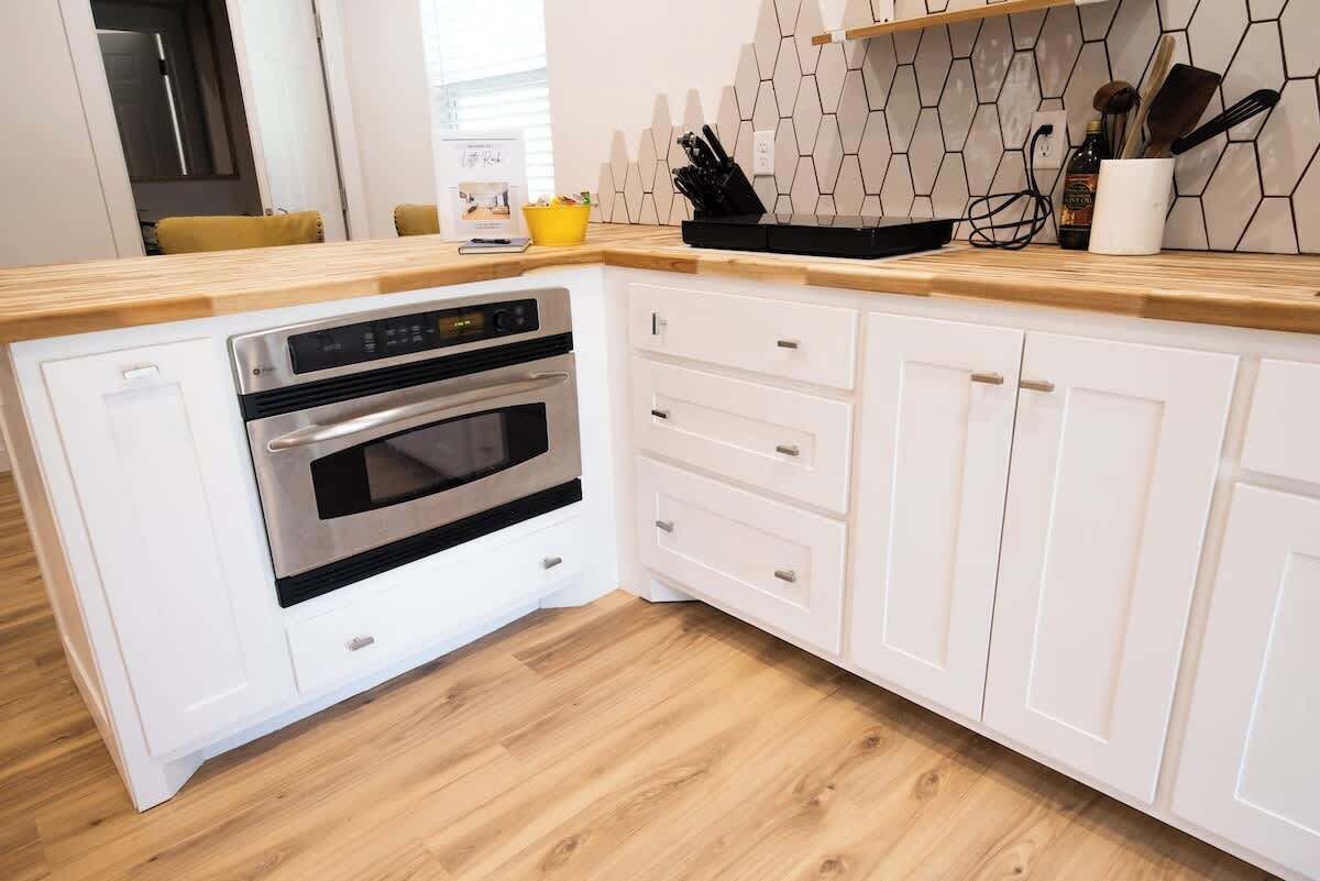 A kitchen with white cabinetry, a wooden countertop, and a built-in oven.