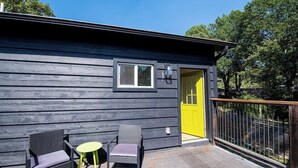 A cabin with a yellow door, two wicker chairs, and a small round table.