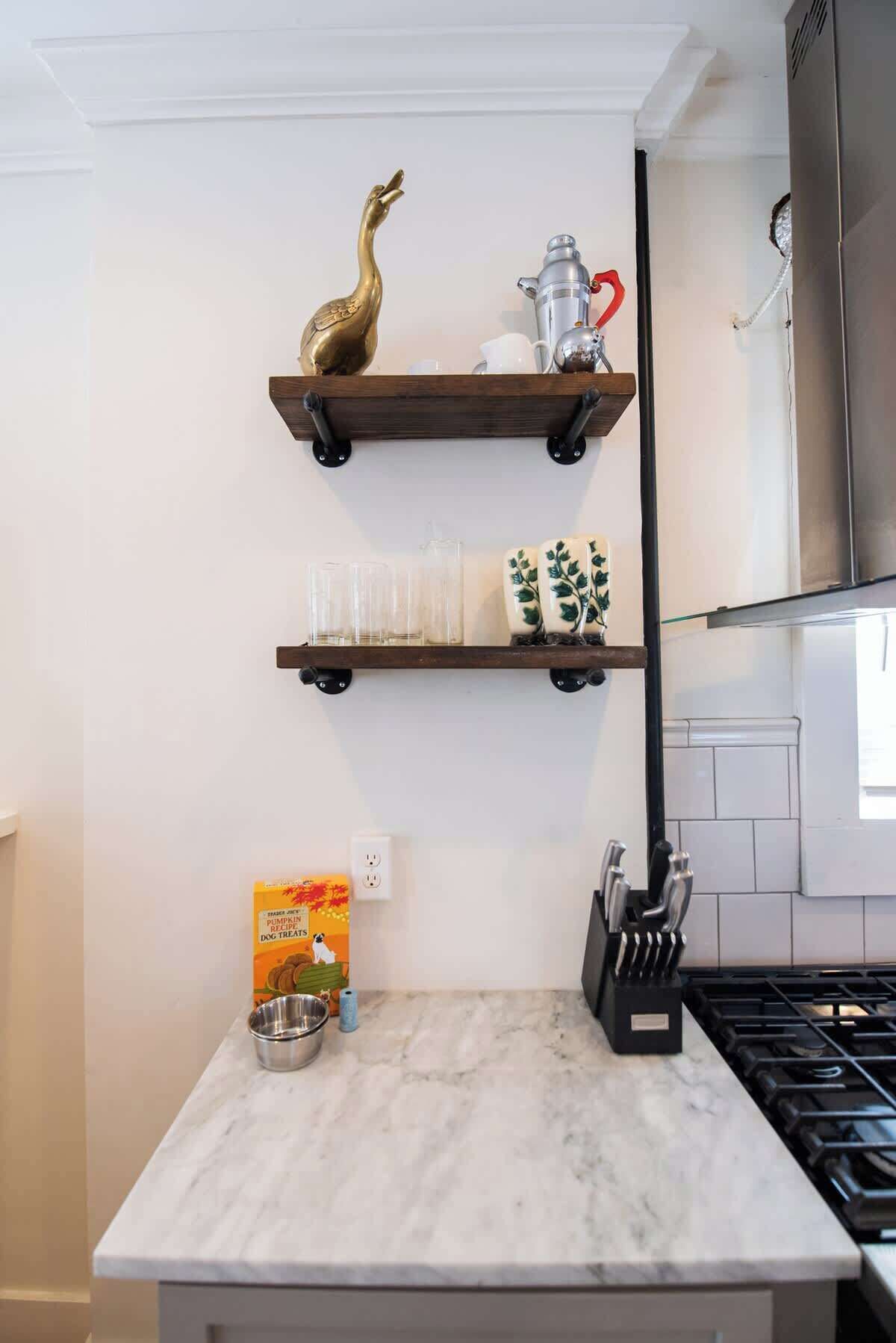 A kitchen with marble countertops, a gas stove, and wall-mounted shelves with decorative items.