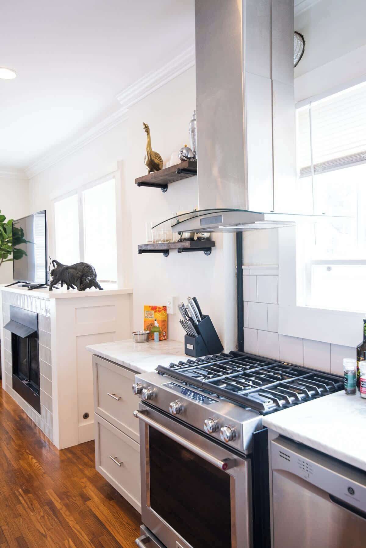Una cucina moderna con piano cottura, forno e lavastoviglie integrate in acciaio inossidabile. Dispensa con mobili in legno, piano di lavoro e finestra che offre luce naturale.
