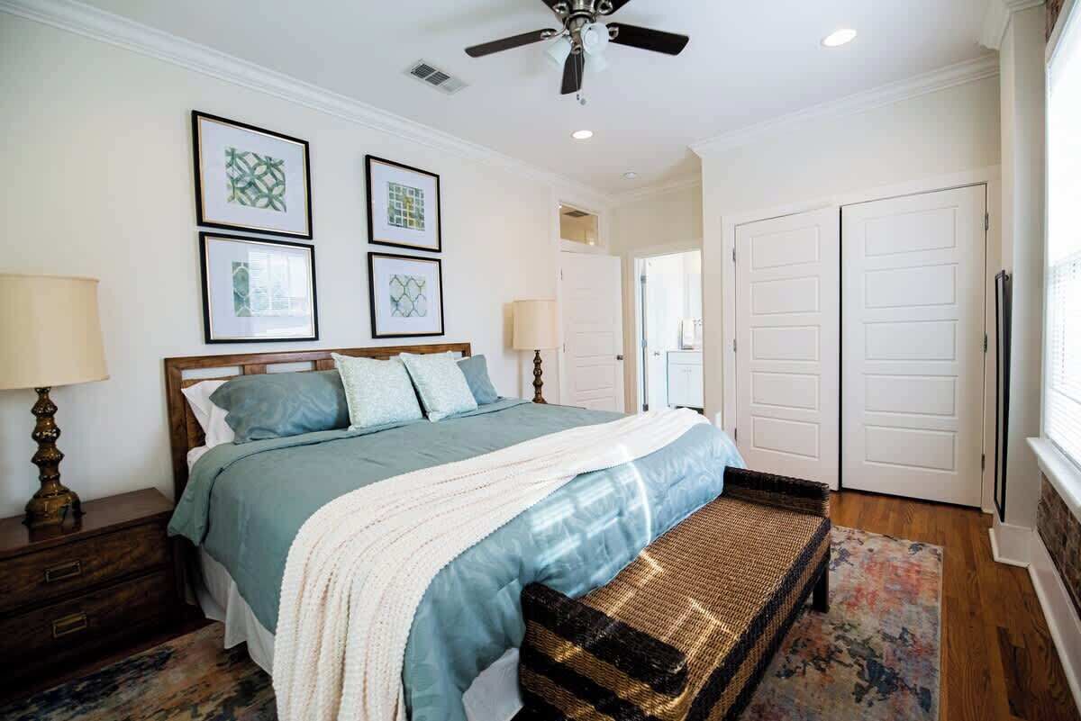 A bedroom with a bed, nightstands, a ceiling fan, framed artwork, and a door.