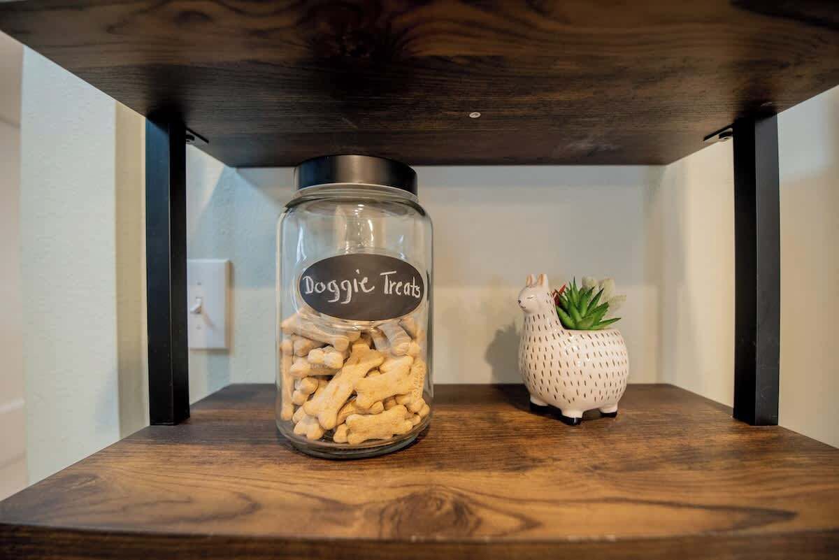 A glass jar labeled 'Doggie Treats' on a wooden shelf.