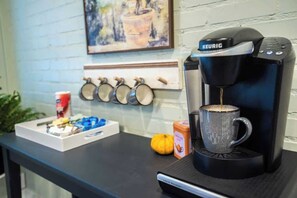 Una cafetera Keurig sobre una mesa con una taza, una calabaza pequeña y una caja de cápsulas de café.