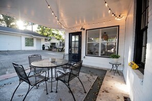 An outdoor patio with a round table and chairs, string lights, and a large window.