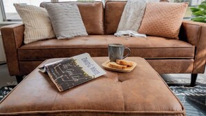 Un canapé en cuir marron, sur lequel repose un livre intitulé « La Belle Vie » et une tasse sur un plateau en bois.