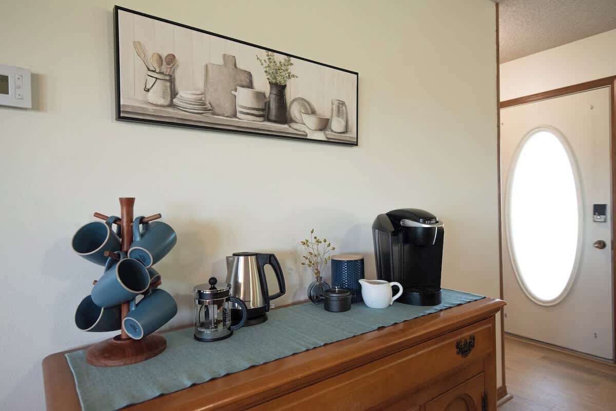 Uma kitchenette com máquina de café, chaleira e caneca sobre um balcão de madeira.