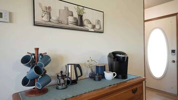 Uma kitchenette com máquina de café, chaleira e caneca sobre um balcão de madeira.