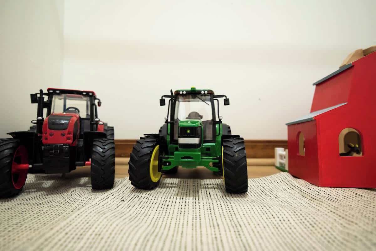 Deux petits tracteurs jouets sont posés sur une surface texturée, avec une structure rouge en arrière-plan.