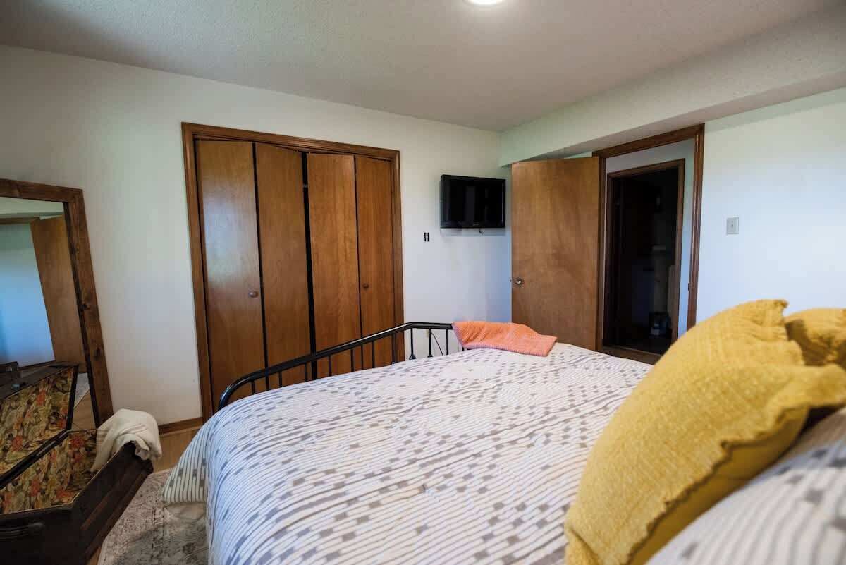 A bedroom with a bed, wooden wardrobe, and a television on the wall.