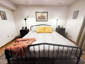 A bedroom with a metal bed frame, a patterned bedspread, two bedside lamps, and a framed picture on the wall. - The Cozy Little Farmhouse (El Paso)