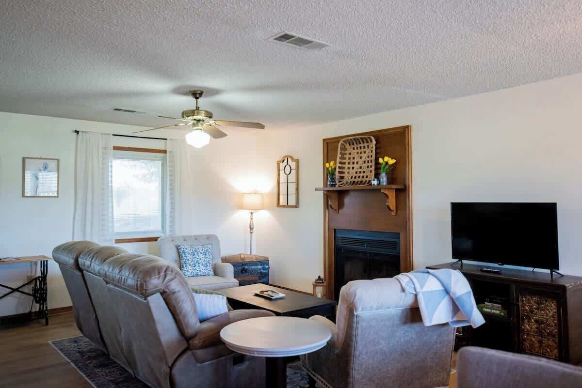 A living room with a sofa, armchairs, a coffee table, a television, a fireplace, and a ceiling fan.