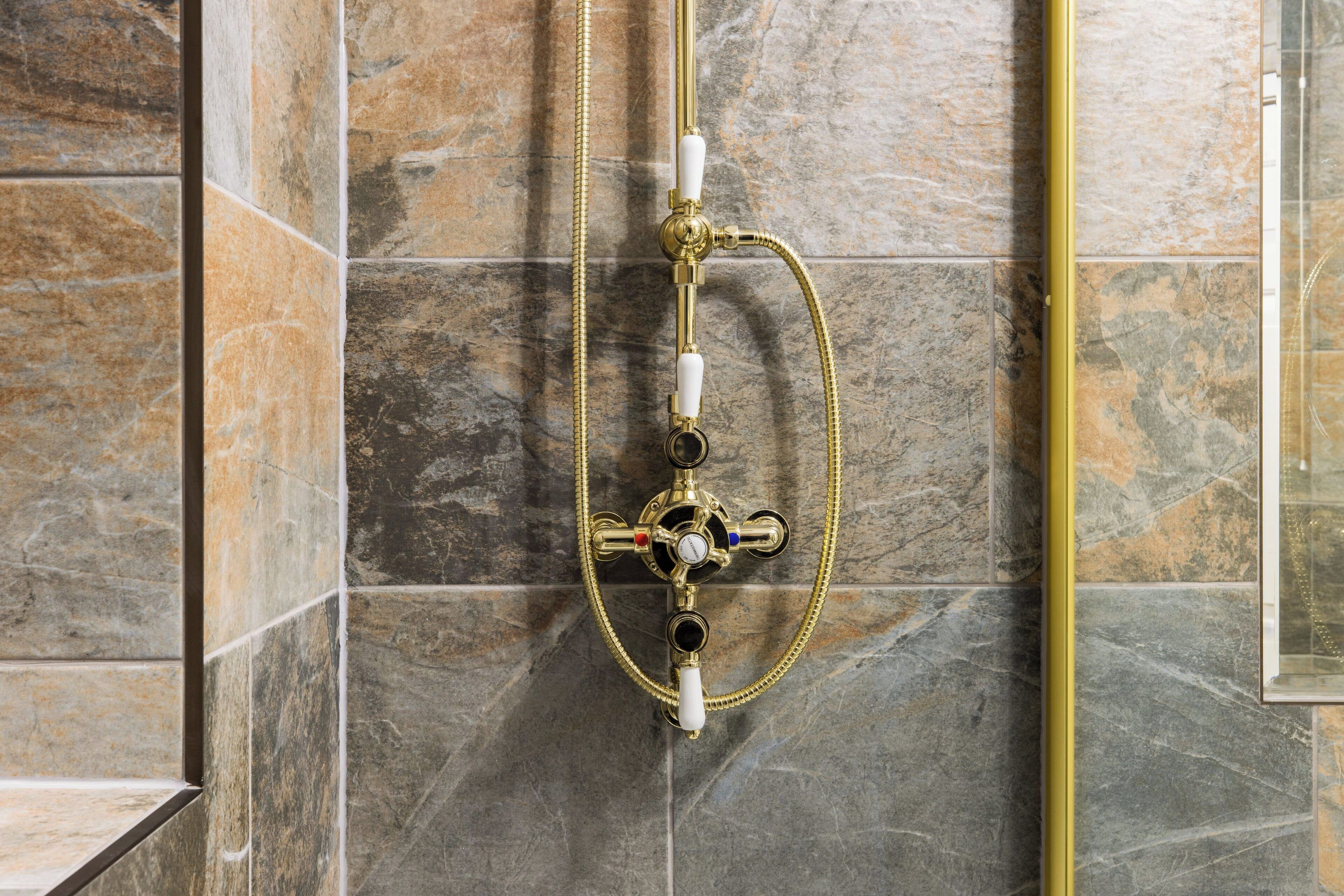 A shower with a gold hose and control knobs against a stone wall.