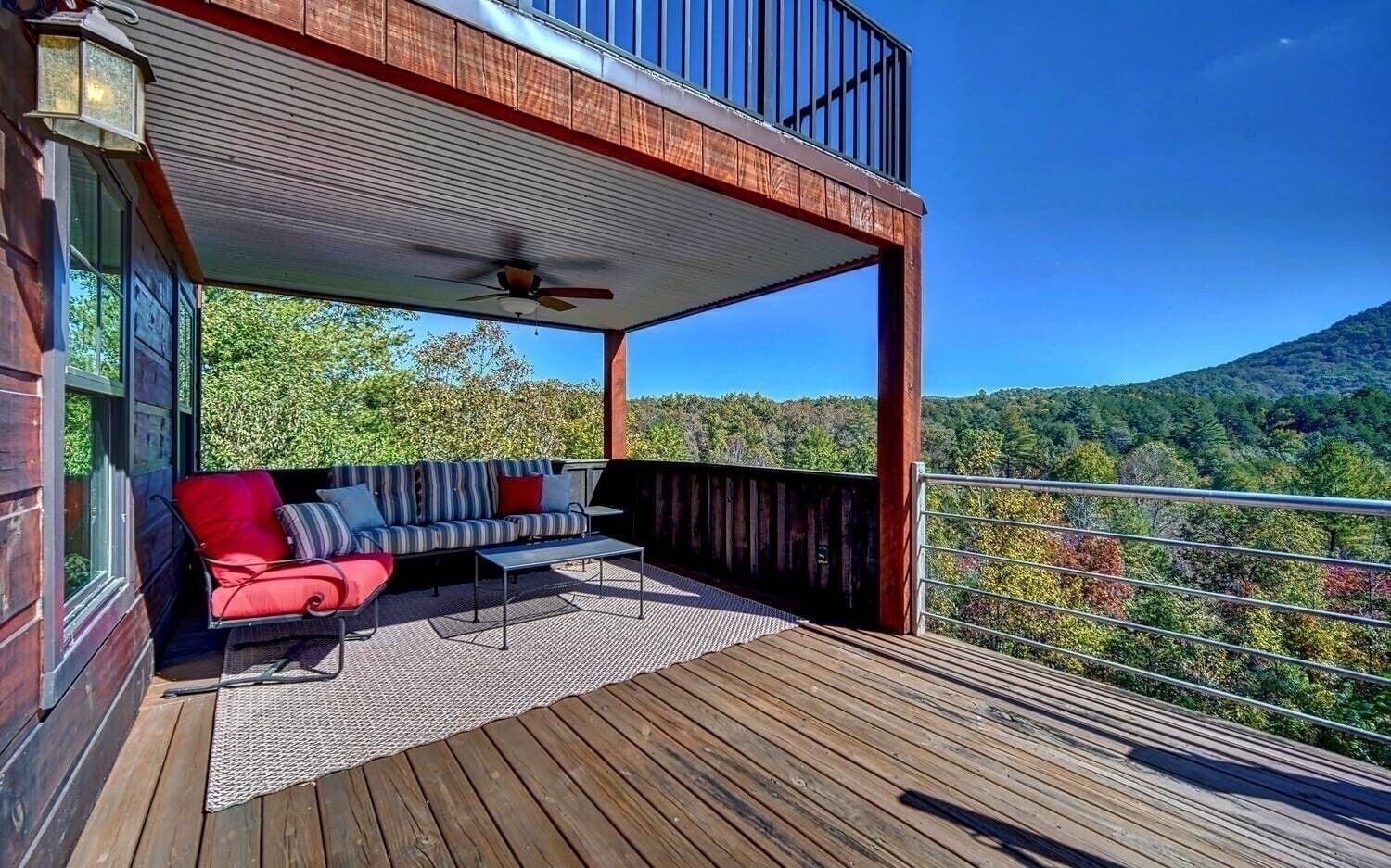 A wooden deck with a sofa and a table, a ceiling fan, and a view of a forested mountain.