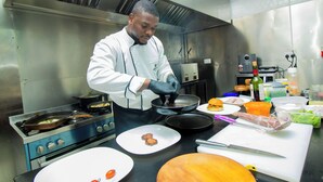 A chef preparing food in a professional kitchen with stainless steel appliances and various cooking utensils. - ArthillsBoutiqueHotel (Kigali)