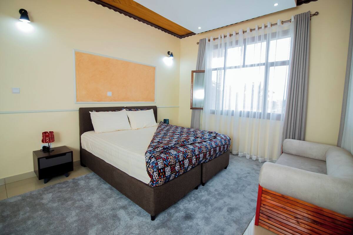A bedroom with a bed, bedside table, lamp, and a chair.
