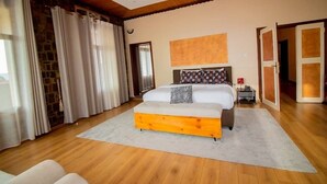 A bedroom with a large bed, wooden flooring, a stone wall, and a view of the outdoors. - ArthillsBoutiqueHotel (Kigali)