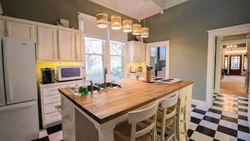 Een keuken met witte kastjes, een houten kookeiland met barstoelen, een zwart-wit geruit vloertje en hanglampen.
