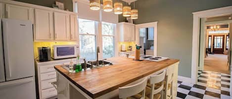 A kitchen with white cabinets, a wooden island with bar stools, a black and white checkered floor, and pendant lights.