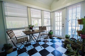 A conservatory with a checkered floor, a wooden table, and chairs, surrounded by potted plants. - Historic Beauty in WLR (Little Rock)