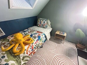 Un dormitori amb un llit, una petita taula de nit, una planta en test i una finestra.