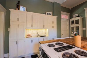 A kitchen with white cabinets, a stove, and a tiled backsplash. - Historic Beauty in WLR (Little Rock)