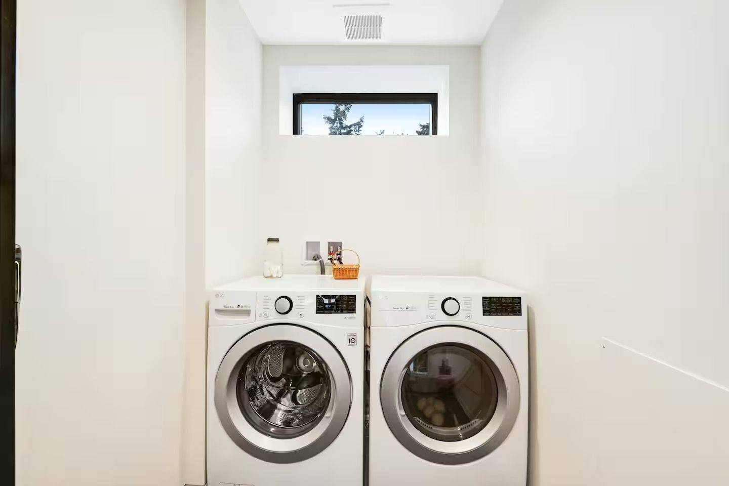A laundry room with two front-loading washing machines, a small window above them, and a white wall.
