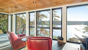 Une chambre moderne avec de grandes fenêtres donnant sur un lac, meublée de fauteuils en cuir et d’une petite table.