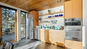 Une cuisine moderne dotée d’appareils électroménagers en acier inoxydable, de meubles en bois et d’une grande fenêtre donnant sur un jardin.