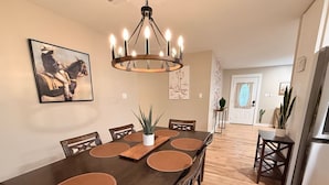A dining area with a long table, chairs, a chandelier, and a potted plant.