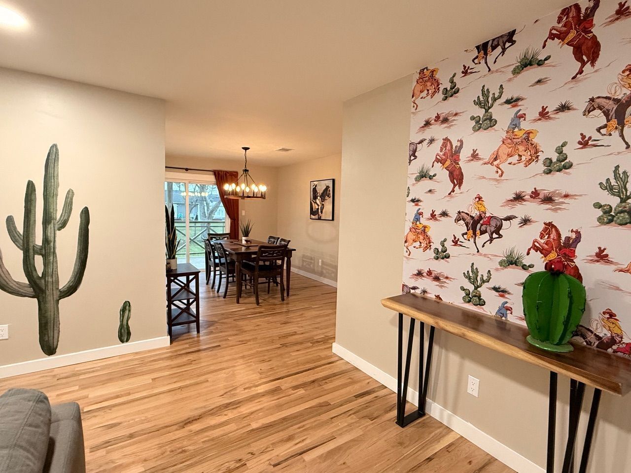 Un vaste espace de vie doté d’un plancher en bois, d’une table à manger avec des chaises et d’un mur orné d’une fresque représentant des cactus.