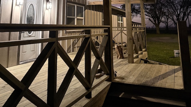 A covered outdoor area with a wooden deck, a metal railing, and a building with large windows and a door.