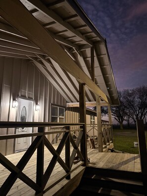 A covered outdoor area with a wooden deck, a metal railing, and a building with large windows and a door. - Casa Bonita Van Vleck, Pet Friendly (Van Vleck)