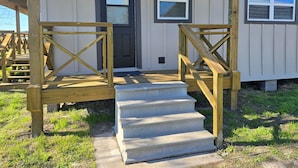 A wooden deck with a concrete staircase leading to a door.