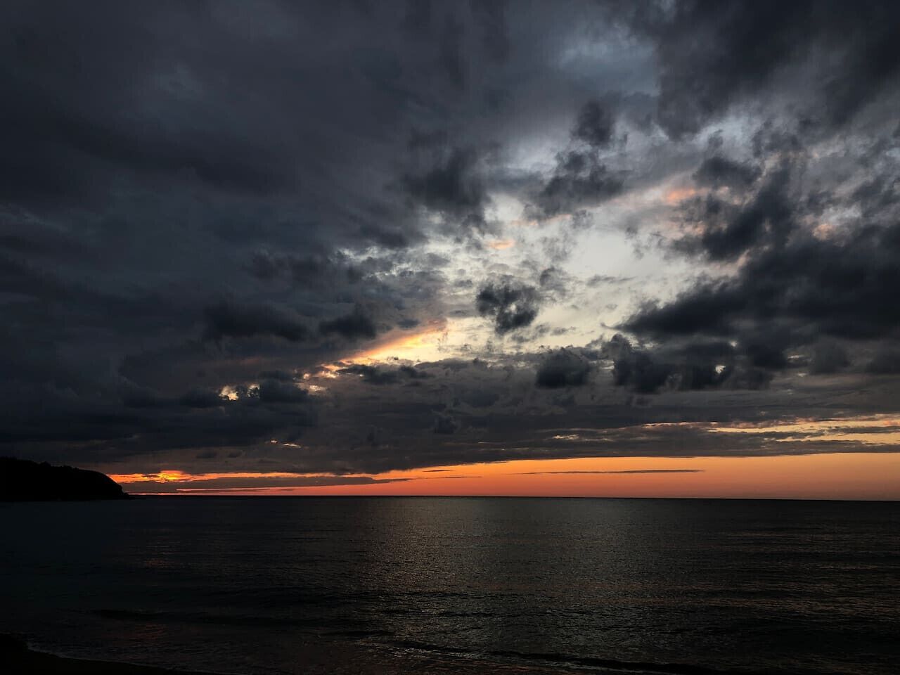 Tramonto su un corpo d'acqua, con la silhouette della terra all'orizzonte.