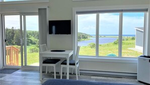Een kamer met een groot raam, een flatscreen televisie, een bureau met twee stoelen en uitzicht op een meer en bos.