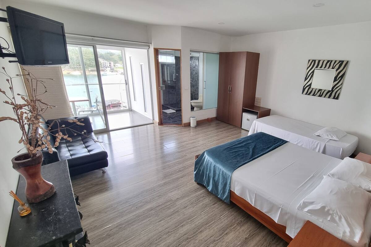 Ein modernes Hotelzimmer mit einem großen Bett, einem Fernseher, einer Couch und Meerblick durch eine Schiebetür.